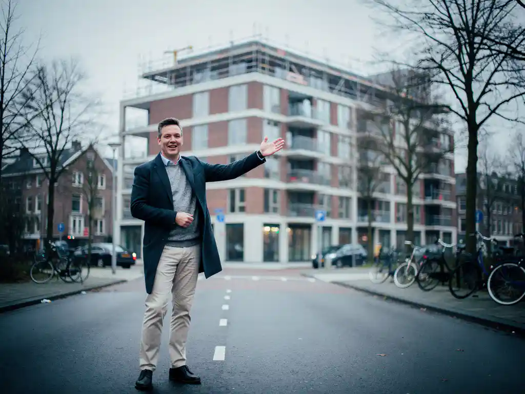 Makelaar in Rotterdam Noord wijst naar nieuwbouwappartementencomplex in aanbouw met steigers, rode baksteen en betonnen gevel.